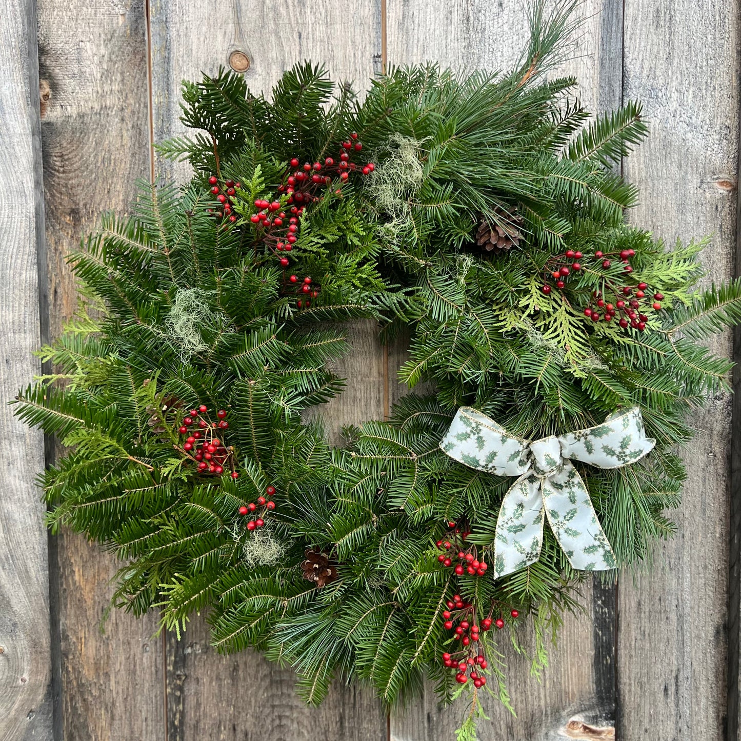 Christmas wreath with greenery, berries, and a bow on a wooden background