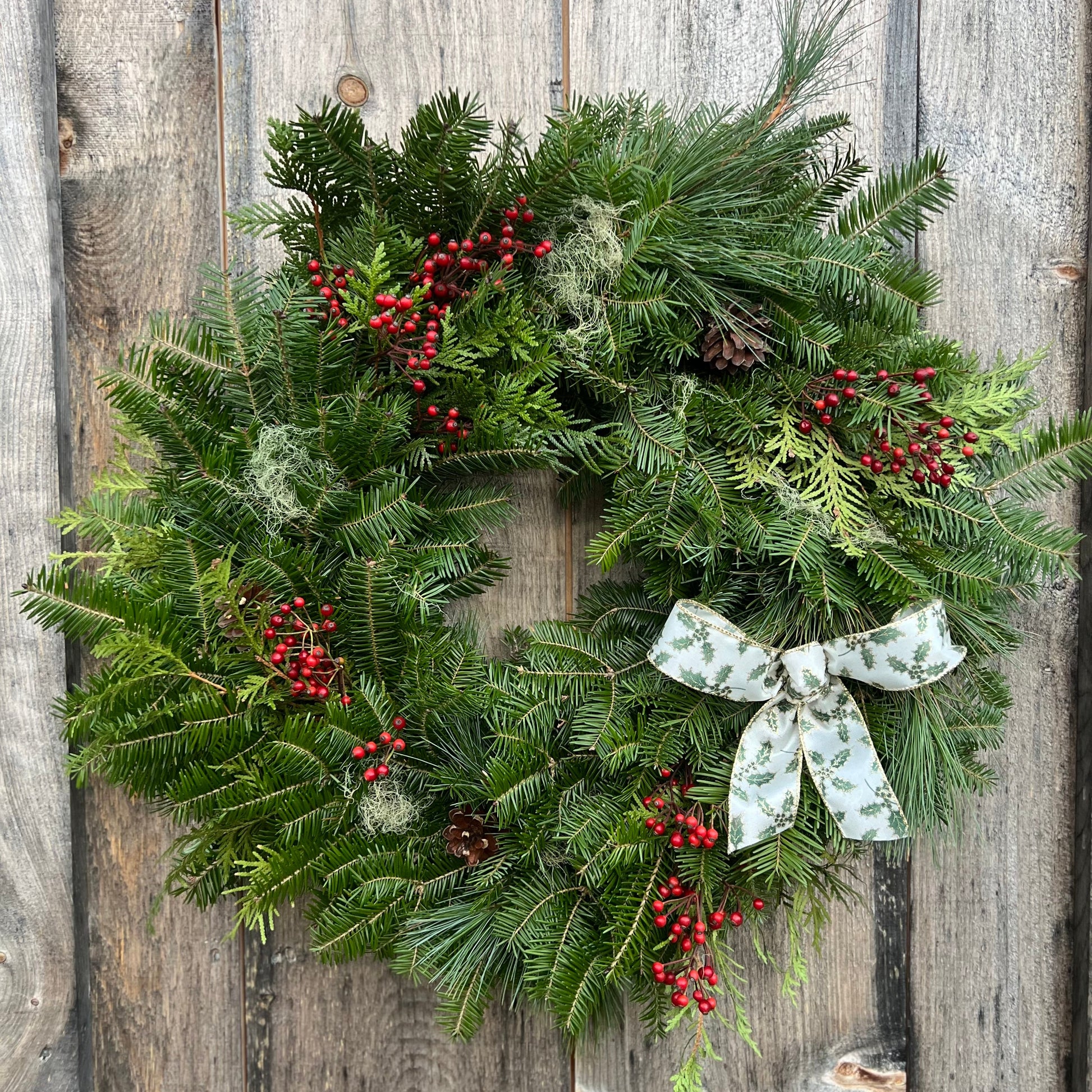 Christmas wreath with greenery, berries, and a bow on a wooden background